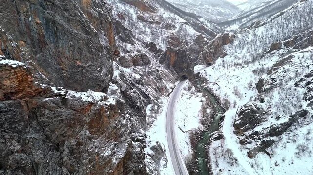 A dramatic aerial view of the snowy canyon walls, winding road and flowing river in Munzur Valley. Ideal for nature, geography, winter landscapes and cinematic drone footage.