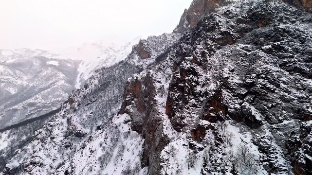 A dramatic aerial view of snowy rocky cliffs and rugged winter mountain terrain in Munzur Valley. Ideal for nature, geography, winter landscapes and cinematic drone footage.