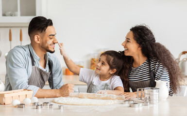Fototapeta premium Happy middle-eastern family playing with flour while making dough for cookies, cheerful father, mother and cute little daughter spending time together, baking pastry at kitchen, panorama