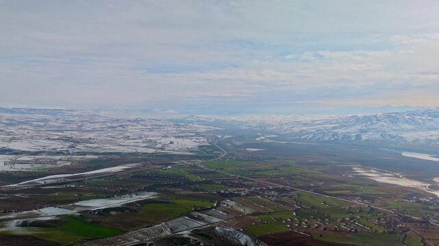 A cinematic aerial view of snowy mountains and partially snow-covered farmlands in Tunceli, Turkey. Perfect for nature, geography, winter landscapes, rural scenery, and drone footage.
