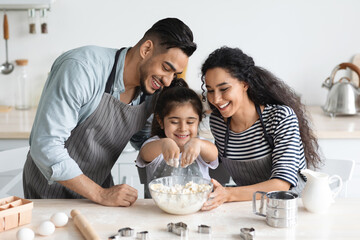 Adorable little girl playing with pastry dough while making delicious cookies with loving parents middle eastern young man and woman, kitchen interior, copy space. Family lifetime concept