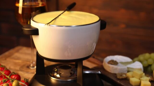 Fondue with tasty melted cheese, snacks and wine on wooden table. Camera moving up