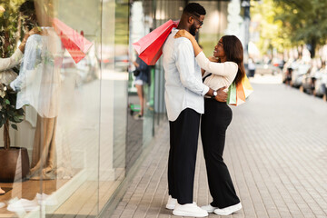 Full body length portrait of cheerful black lady hugging her boyfriend standing outdoors, holding...