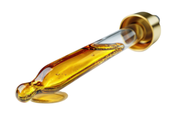 Close up of a glass dropper with golden liquid spilling onto a black surface