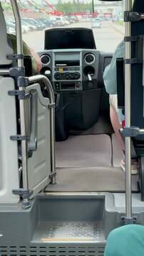 Van interior cockpit with driver hands. on wheel, open side door showing textured floor mat and metal step, dashboard gauges and monitor visible, parking lot beyond windshield,