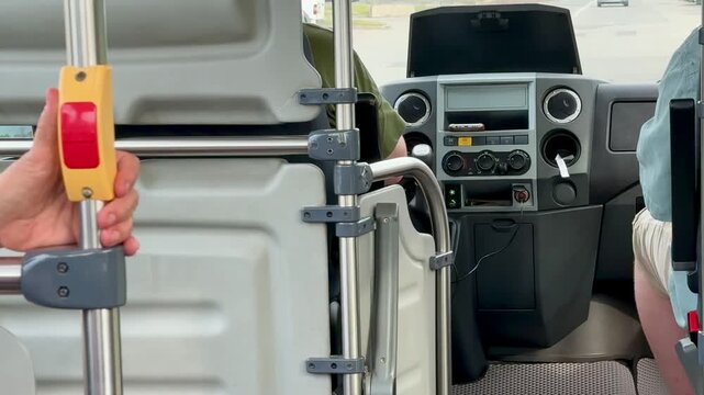 Van interior cockpit with driver hands. on wheel, open side door showing textured floor mat and metal step, dashboard gauges and monitor visible, parking lot beyond windshield,