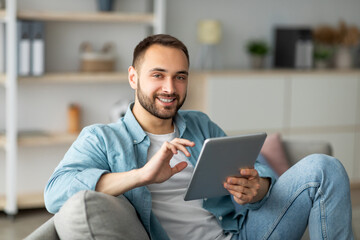 Online life concept. Happy young man using tablet computer, working or studying from home. Handsome...