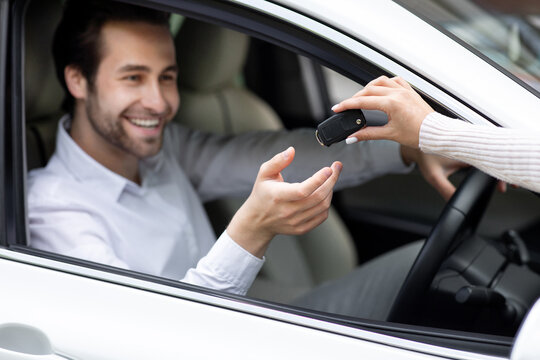 Choosing new auto at dealership. Businessman have agreed to buy, sell new transport in motor show. With special privilege promotion seller give key to young cheerful european man in shirt in white car
