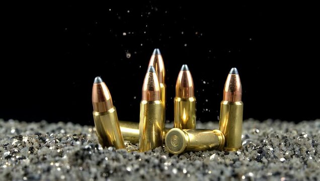 High quality 4K slow motion close up of golden 9mm bullets falling bouncing on textured silver black sand surface emphasizing motion metallic reflections cinematic visual 
