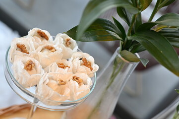 Artisanal walnut sweets in white floral paper liners, elegant wedding dessert table with glass stand, close up of gourmet nut confections for reception, sophisticated party sweets display
