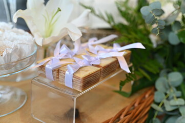 Traditional Brazilian Bem-Casado wedding favors with lilac ribbons, elegant sweets display on acrylic stand for reception, close up of tiered sponge cake treats with floral background