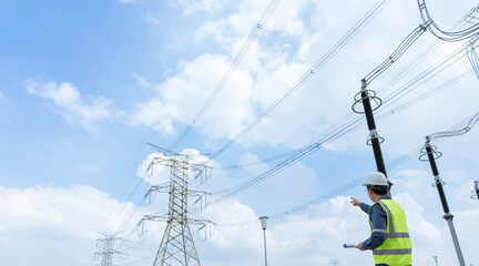 Professional electrical engineer in safety vest and hardhat inspecting high voltage power lines and...