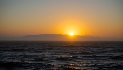 The image depicts a tranquil ocean scene at sunset, with the sun partially visible as it dips behind a distant mountain range
