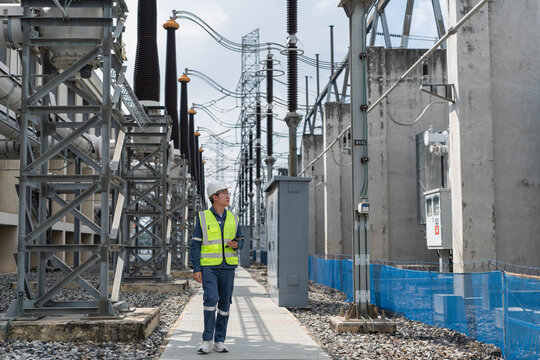Professional electrical engineer walking through power substation switchyard for routine inspection of high voltage insulators and industrial electrical infrastructure equipment.