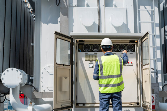 Engineer inspecting transformer control panel at power substation, monitoring electrical equipment and ensuring safe and reliable operation of high voltage energy infrastructure.