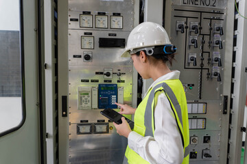 Female electrical engineer operating protection relay and control system on indoor panel while...