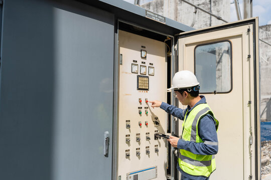 Male electrical engineer hand pressing button on marshalling cubicle control panel at power substation, using digital tablet for remote monitoring and industrial grid maintenance.