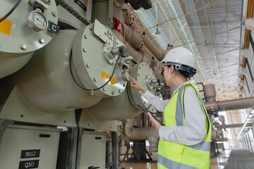 Female engineer in hardhat using tablet to inspect high voltage gas insulated switchgear equipment in substation. Professional inspector monitoring industrial energy system pressure. © JD Studio