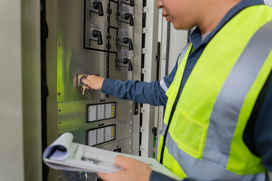 Electrical engineer operating a control panel inside a substation, using a checklist to verify system status, safety procedures, and operational readiness for reliable power distribution.