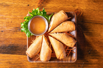 A plate of Asian spring rolls with spicy dipping sauce on a wooden table