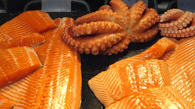 Close up view of fresh raw seafood on a market counter, showing vibrant orange salmon fillets and octopus tentacles ready for sale, highlighting healthy eating and gourmet ingredients