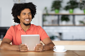 Portrait Of Happy Black Young Guy Relaxing At Cafe With Digital Tablet And Coffee, Smiling Millennial African American Man Sitting At Table With Tab Computer In Hands And Looking Away, Copy Space