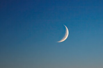 Crescent moon illuminated in the early evening, set against a gradient blue sky