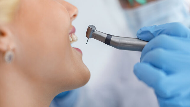 Cropped of young smiling blonde woman and dentist hands in blue robber gloves with dental drill, side view, panorama. Unrecognizable female patient visiting dentistry, having regular checkup