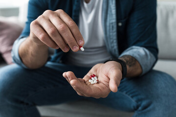 Fototapeta premium Colorful pharmaceutical medicine pills, narcotic drugs in capsules on palm. Man holding medicine at home. Sad unhappy millennial european guy holding many different pills in hand, close up, cropped