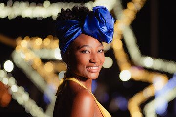 African caribbean woman smiling wearing blue headwrap at night