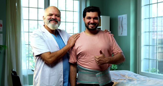Indian physiotherapist with happy patient with back pain smiling and showing thumbs up using lumbar support as experienced male therapist stands inside modern Indian clinic OPD healthcare visit