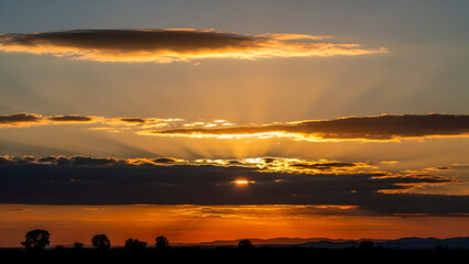 Beautiful dramatic sunset sky with golden sun rays breaking through dark clouds over horizon