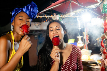 Diverse friends enjoying street food candy apples at night