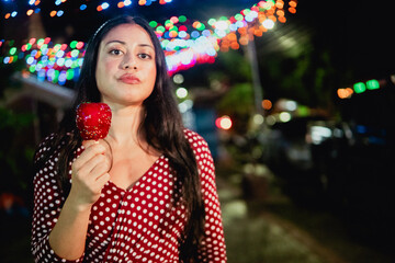 Young hispanic woman enjoying candy apple at night fair