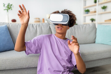 Modern domestic hobbies. African American teen guy in virtual reality headset touching imaginary screen, exploring cyberspace at home. Black adolescent in VR glasses playing interactive video game