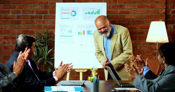 Indian businessmen clapping on presentation as group of senior Indian Asian business leaders and higher management celebrate successful growth projection using chart in cozy modern office