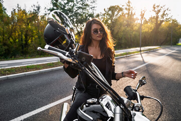 Attractive girl sitting on motorcycle with helmet in her hands enjoying sunset after long ride