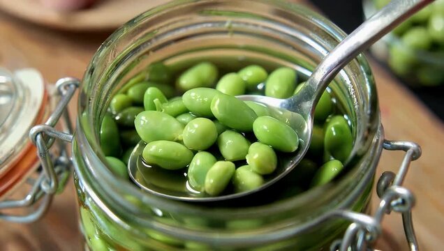 Cinematic 4K top down footage of spoon scooping canned green pea kernels rotating to show marinated pickled peas emphasizing color texture culinary 