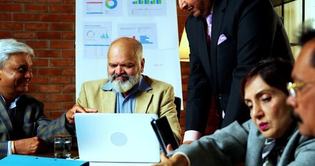 Indian senior business people working in office together as group of senior Indian Asian businessmen collaborate using laptop, papers at desk while analyzing tasks in cozy modern corporate workplace - Powered by Adobe