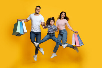 Seasonal Sales Concept. Happy Middle Eastern Family Of Three Jumping With Shopping Bags Over Yellow...