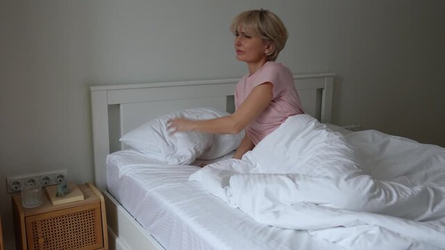 Middle aged woman sleeping waking up irritated by loud noises outside, looks at window, falling back to sleep with tired exhausted expression. Female trying to sleep with noisy sounds from street.