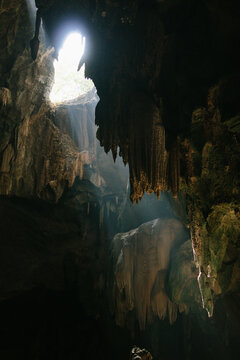 Inside Tham Chomphon, a sinkhole lets sunlight filter in, highlighting ancient stalactites. This famous Ratchaburi cave offers stunning geological views.