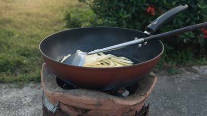 Close-up top view of french fries deep frying in hot boiling oil. Yellow potato sticks cooking in a black wok. Unhealthy fast food and snack concept.