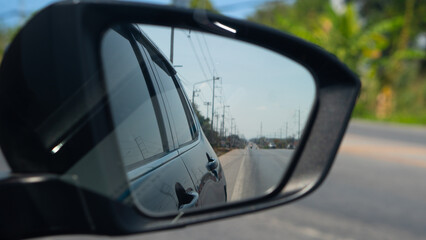 Car side mirror view reflecting the asphalt road and blue sky. Transportation, travel, and driving safety concept. Traffic conditions are clear. with electric pole side of road in Thailand.