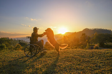 Silhouette of male in a wheelchair playing with his Golden Retriever dog together on mountain sunset , a touching scene of companionship, loyalty, and hope