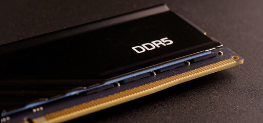 Macro shot of a DDR5 RAM stick showing the heat sink and circuit board on a dark surface. Concept of expensive electronic shortages and modern technology prices. Photo.