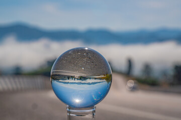 A serene landscape of fog, mountains, and open road seen through a crystal ball, expressing imagination and new perspectives. Through the Glass A Journey Into the Mist Covered Valley