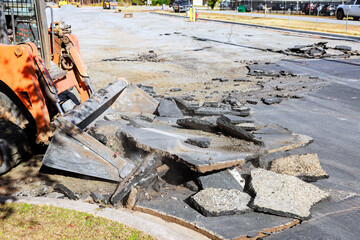 Heavy machinery removes asphalt from damaged road at construction site