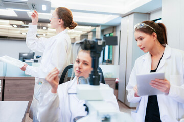 Fototapeta premium Diverse team of female scientists working in busy digital pathology lab. Researchers analyzing histology slides using microscope, tablet, and visual inspection for medical diagnosis.