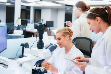 Diverse team of female scientists working in busy digital pathology lab. Researchers analyzing histology slides using microscope, tablet, and visual inspection for medical diagnosis.